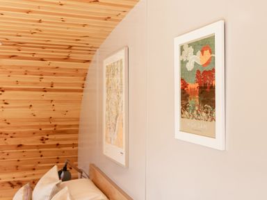A bedroom wall with two framed pictures above a bed with pillows and a reading lamp at Little Heaning in Cartmel