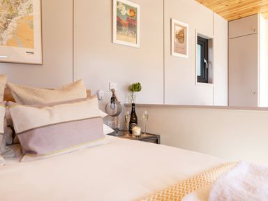 A bedroom with a bed a side table with a bottle and two glasses on it and framed pictures on the wall at Little Heaning in Cartmel
