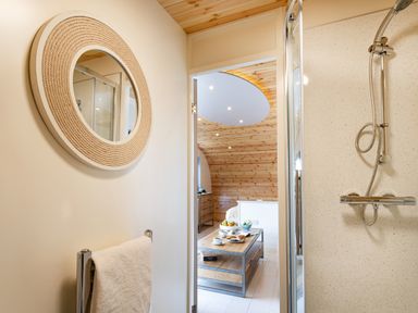 A bathroom with a round mirror towel rack and shower looking into a bedroom with wooden ceiling and a table with breakfast at Little Heaning in Cartmel