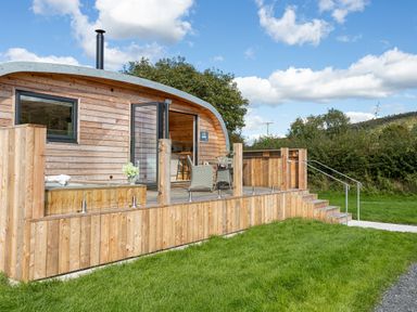 A wooden cabin with a curved roof and an outdoor deck with chairs and a table at Little Heaning in Cartmel