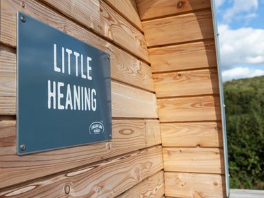 A wooden exterior wall with a blue sign reading Little Heaning and greenery in the background at Little Heaning Cartmel