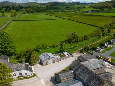 A rural farm setting with green fields and several buildings including a house, barns, and pods at Little Heaning in Cartmel