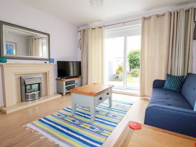 A living room with a fireplace television coffee table sofa and sliding glass door at 6 Ocean Heights in Newquay