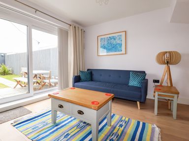 A living room with a blue sofa two cushions a wooden coffee table a side table with a lamp and striped rug at 6 Ocean Heights in Newquay
