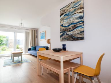 A dining area with a wooden table and yellow chairs next to a living room with a blue sofa and coffee table at 6 Ocean Heights in Newquay