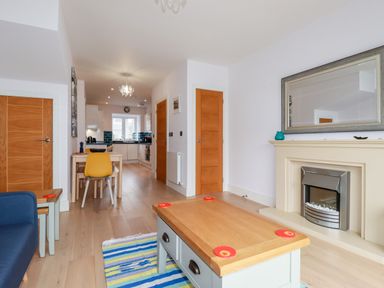 A living room with a fireplace a wooden coffee table a striped rug a blue chair and a dining table with a yellow chair at 6 Ocean Heights in Newquay