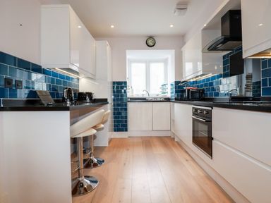 A kitchen with white cabinets blue tile backsplash and wooden floor at 6 Ocean Heights in Newquay