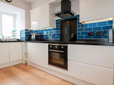 A kitchen with white cabinets blue tiled backsplash black countertop and black oven at 6 Ocean Heights in Newquay