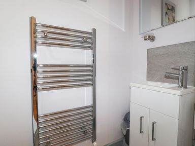 A bathroom with a chrome towel radiator next to a white sink cabinet and a mirror at 6 Ocean Heights in Newquay