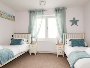 A bedroom with two single beds with blue cushions and throws separated by nightstands with lamps at 6 Ocean Heights in Newquay
