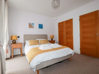 A bedroom with a bed with yellow pillows and a yellow throw two bedside tables with lamps wooden doors and two framed pictures on the wall at 6 Ocean Heights in Newquay
