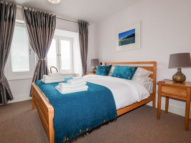 A bedroom with a wooden bed frame a blue throw and pillows two bedside tables with lamps and curtains at 6 Ocean Heights in Newquay