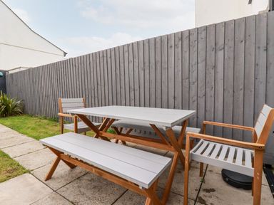 An outdoor patio area with a table bench and two chairs next to a gray wooden fence at 6 Ocean Heights in Newquay