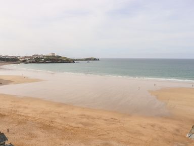 A wide sandy beach with a calm sea and distant hill with buildings at 6 Ocean Heights in Newquay