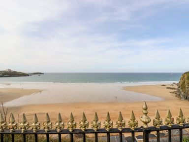 A view of a sandy beach and ocean behind a decorative metal fence at 6 Ocean Heights in Newquay