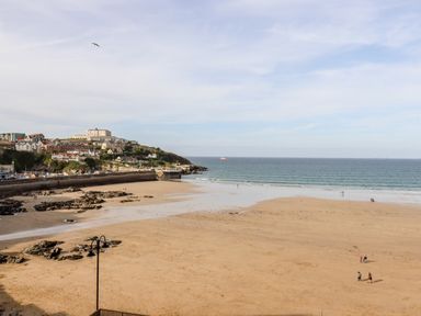 A sandy beach with rocks and a few people near the shoreline and houses on a hill in the background at 6 Ocean Heights in Newquay