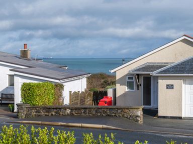 A view of houses with a stone wall and ocean in the background at Cartref in Benllech