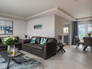 A living room with two sofas a coffee table with flowers and champagne glasses and a dining area with chairs and a table at Cartref in Benllech