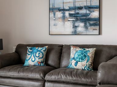 A brown leather sofa with two sea creature cushions and a painting of boats on the wall at Cartref in Benllech