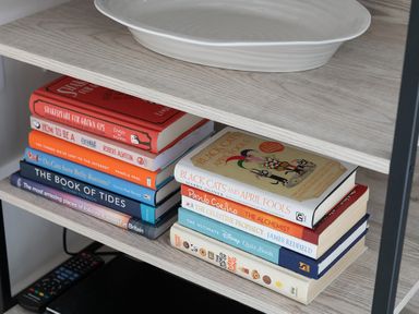 A shelf with two stacks of books and a white dish on a wooden shelf at Cartref in Benllech