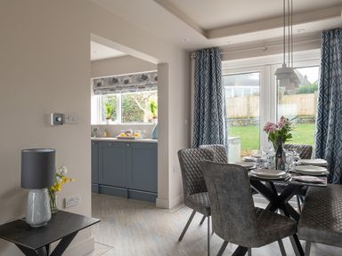 A dining area with a table set with plates and glasses next to a window with patterned curtains and a view of a garden at Cartref in Benllech