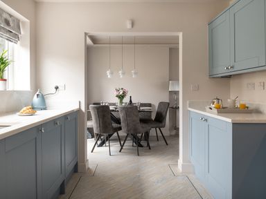 A kitchen with blue cabinets and a dining area with a table and gray chairs at Cartref in Benllech