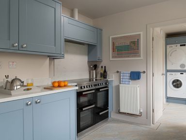 A kitchen with blue cabinets a stove oranges on a cutting board and a laundry area with a washer and dryer at Cartref in Benllech