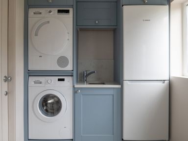 A laundry area with a stacked washing machine and dryer a small sink with blue cabinetry and a white refrigerator with a window nearby at Cartref in Benllech