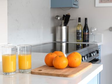 A kitchen countertop with five oranges on a wooden cutting board and two glasses of orange juice at Cartref in Benllech