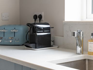 A kitchen counter with a blue toaster black coffee machine chrome faucet and soap dispenser at Cartref in Benllech