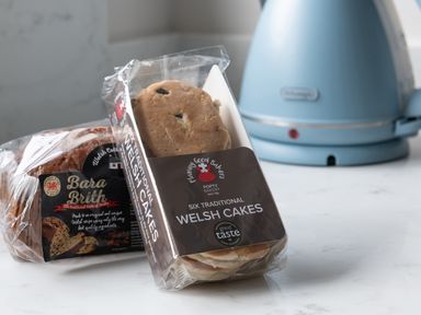 A kitchen counter with a blue kettle and packaged traditional Welsh cakes and Bara Brith bread at Cartref in Benllech