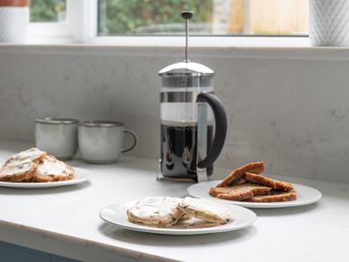A kitchen counter with two mugs and plates of bread near a French press at Cartref in Benllech