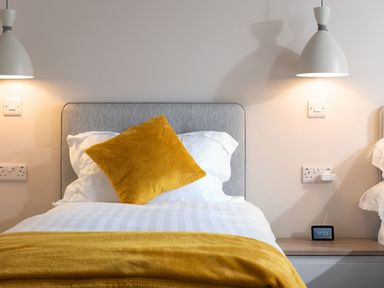 A bed with a yellow pillow and yellow blanket under white lamps in a bedroom at Cartref in Benllech