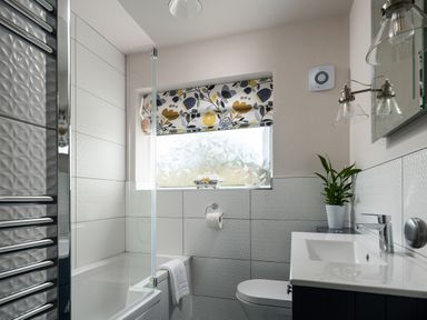A bathroom with a bathtub a toilet a sink a plant and a window with patterned blinds at Cartref in Benllech