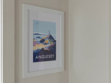 A framed poster of Anglesey with a lighthouse on a gray wall at Cartref in Benllech