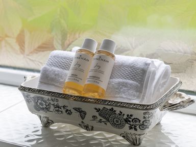 Two small bottles of shampoo and wash with white towels in a decorative ceramic tray on a windowsill at Cartref in Benllech