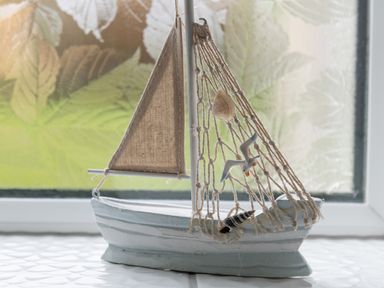 A decorative model of a sailboat with fabric sails and netting with shells and a bird on a windowsill at Cartref in Benllech