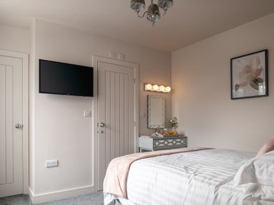 A bedroom with a bed a bedside table with a mirror and a mounted TV on the wall at Cartref in Benllech