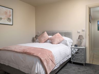 A bedroom with a bed with pink pillows and blanket and a mirrored bedside table at Cartref in Benllech