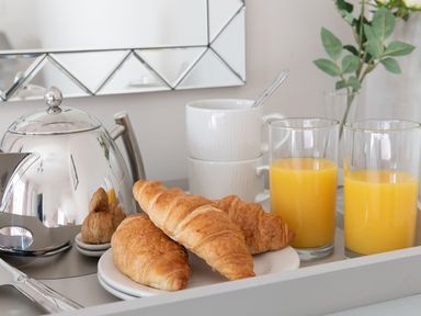 A breakfast tray with croissants two glasses of orange juice a silver teapot stacked white cups and a small vase with green leaves at Cartref in Benllech