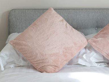 A bed with white sheets and two pink pillows against a gray headboard at Cartref in Benllech