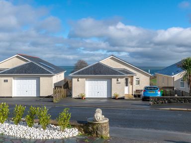 A street view of detached houses with garages and a blue car with the sea in the background at Cartref in Benllech