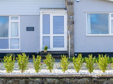 The front entrance of a house with a white door bushes planted in white stones in front of the house at Cartref Benllech