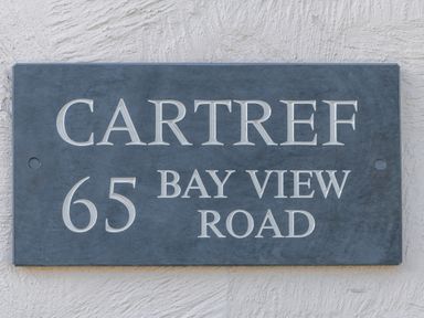 A sign on a wall displaying Cartref 65 Bay View Road at Cartref in Benllech