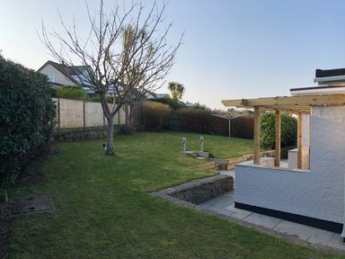 A backyard with a leafless tree a wooden pergola grass and neighboring houses at Cartref in Benllech