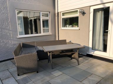 An outdoor patio area with a wicker corner sofa and table next to windows and a glass door at Cartref in Benllech