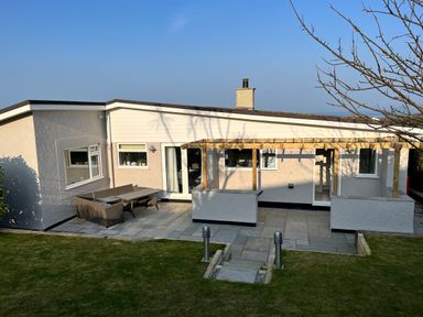A single story house with patio furniture and a wooden pergola on a paved patio at Cartref in Benllech