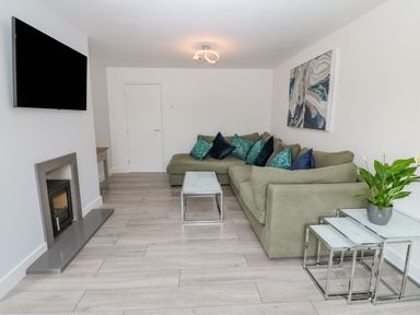 A living room with a green sectional sofa and blue pillows a mounted TV a fireplace and nesting tables with a plant at Daresfield in Cemaes Bay
