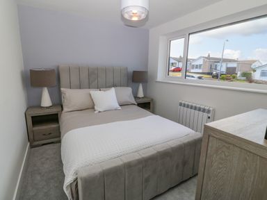 A bedroom with a bed pillows bedside tables lamps a window and a dresser at Daresfield in Cemaes Bay