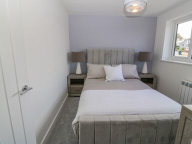 A bedroom with a bed a headboard two bedside tables lamps and a window at Daresfield in Cemaes Bay
